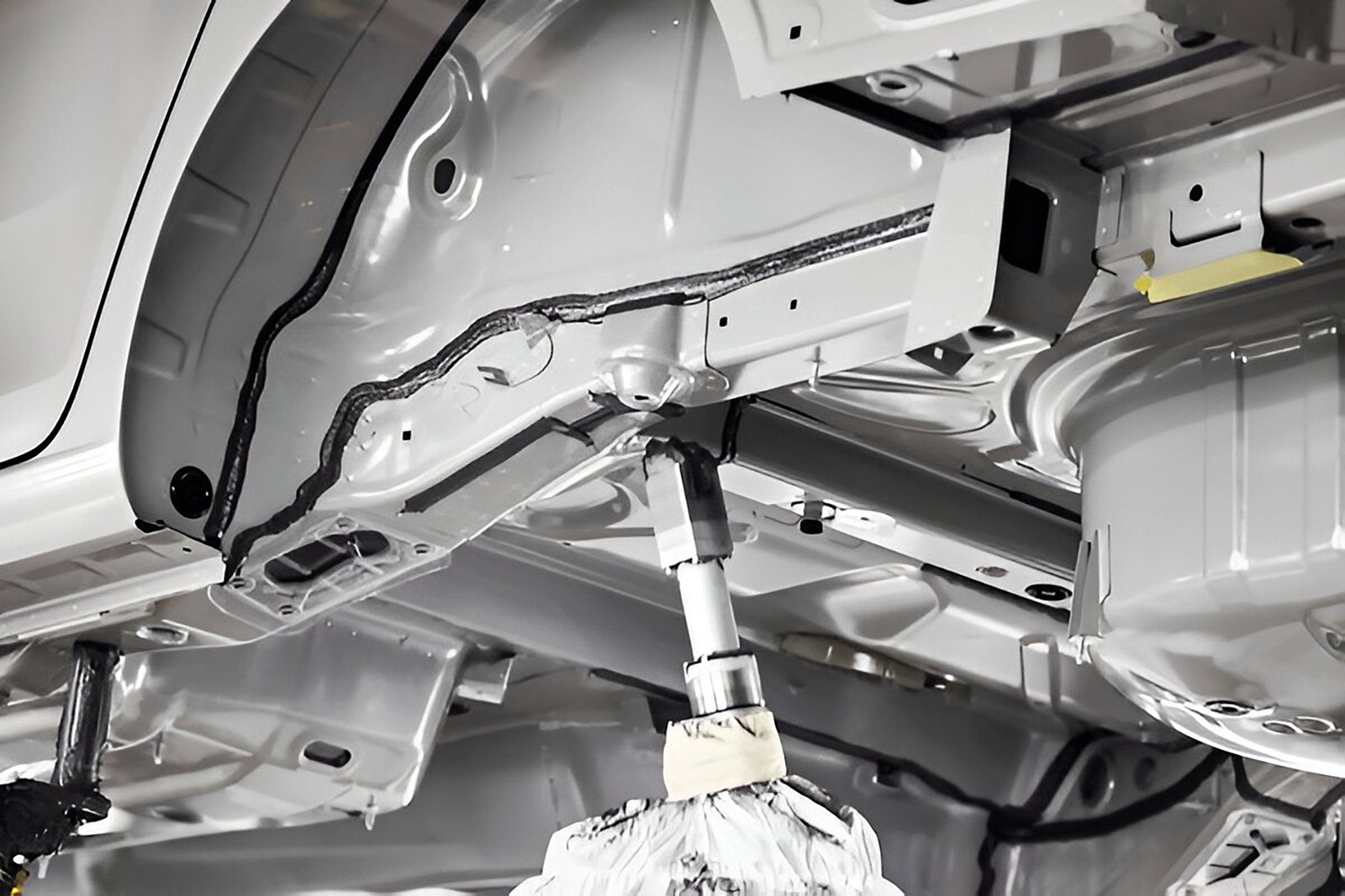 Robo aplicando selante na parte de baixo de um carro pronto para inspeção de adesivo ou selante na linha de produção automatizada